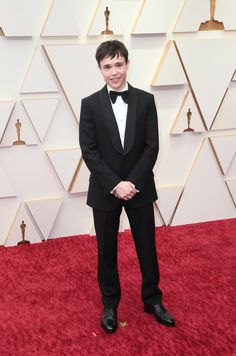 a young man in a tuxedo and bow tie standing on the red carpet