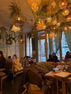 people sitting at tables in a restaurant with plants hanging from the ceiling