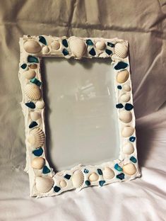 a white frame with seashells and sea glass on the bottom is sitting on a bed