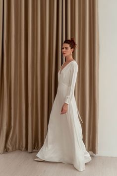 a woman standing in front of a curtain wearing a white wedding dress with long sleeves