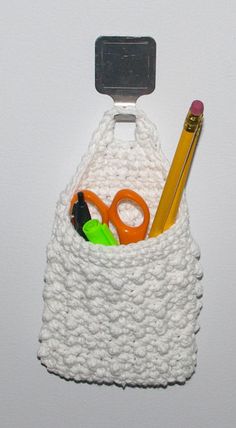 a crocheted purse with scissors, pencils and other items in the pocket