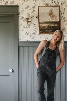 a woman leaning against a wall with her hands on her hips and looking at the camera