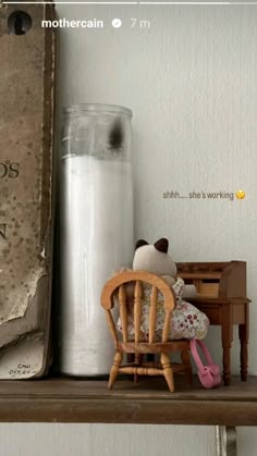 a doll sitting on a chair next to a book and a glass bottle with milk in it