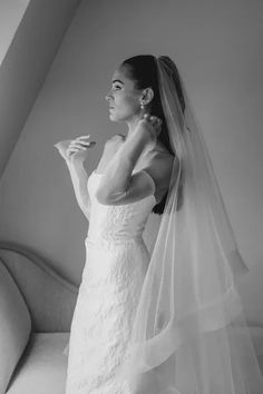 a woman in a wedding dress standing next to a couch and looking at something on her finger