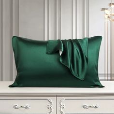 a green pillow with a bow on it sitting on top of a white dresser next to a chandelier