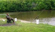 a man sitting in a chair next to a lake with fishing rods and buckets