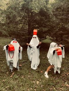 three people dressed in white and red are walking through the woods with orange buckets on their heads