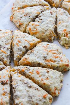 several biscuits with cheese and carrots are arranged on a piece of white parchment paper