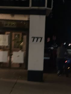 a man riding a motorcycle down a street next to a tall white building at night