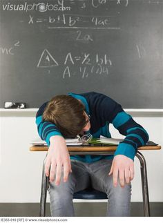 a young boy sitting at a desk in front of a blackboard