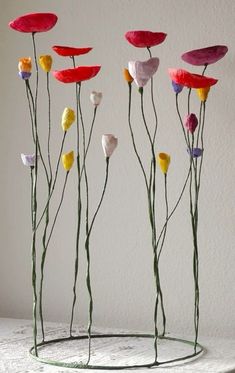 three metal vases with flowers in them sitting on a white counter top next to a wall