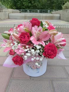 a bouquet of pink and red flowers in a white vase on a brick walkway next to steps