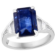 A stunning well-crafted engagement ring showcasing a 5.11-carat emerald-cut Blue Sapphire. Flanking the center diamond are perfectly matched graduating step-cut diamonds, channel set in a polished platinum mounting. 6 Accent diamonds weigh 0.68 carats total. Handcrafted in our New York City workshop. Style available in different price ranges. Prices are based on your selection. Please contact us for more information. Luxury Emerald Cut Ring With Channel Set, Luxury Emerald Cut Channel Set Ring, Formal Sapphire Ring With Diamond Side Stones, Gia Certified Square Cut Sapphire Ring For Formal Occasions, Classic Gia Certified Radiant Cut Sapphire Ring, Formal Sapphire-colored Diamond Ring With Emerald Cut, Classic Emerald-cut Sapphire Diamond Ring, Classic Gia Certified Emerald Cut Sapphire Ring, Formal Emerald Cut Sapphire Ring With Diamond