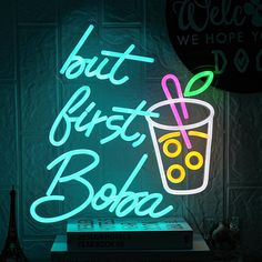 a neon sign that reads, but first booze next to a stack of books