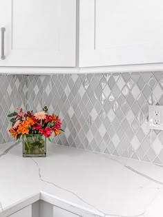 a vase filled with flowers sitting on top of a kitchen counter next to white cabinets