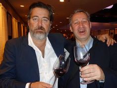 two men holding wine glasses in their hands and posing for the camera with each other