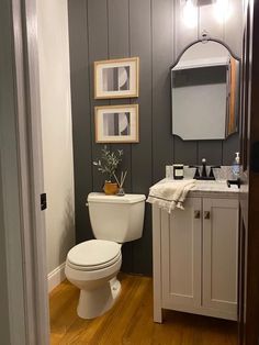 a white toilet sitting in a bathroom next to a sink and wooden floors with framed pictures on the wall