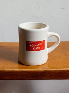 a white coffee cup sitting on top of a wooden table with a red label that says melholad coffee