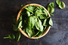 a bowl filled with green leaves on top of a table