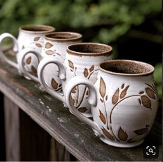 four coffee mugs sitting on top of a wooden rail with leaves painted on them