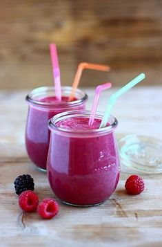 two glasses filled with raspberry smoothie on top of a wooden table next to berries