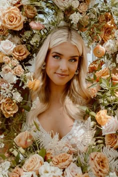 a woman with blonde hair standing in front of an arrangement of flowers and greenery