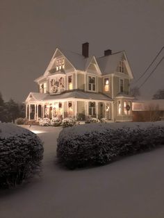 a large white house sitting on top of a snow covered hill next to a lush green hedge