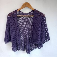 a purple crocheted sweater hanging on a wooden hanger