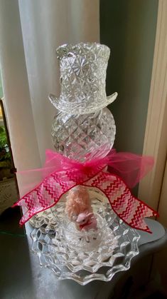 a small teddy bear sitting on top of a glass cake plate with a pink bow