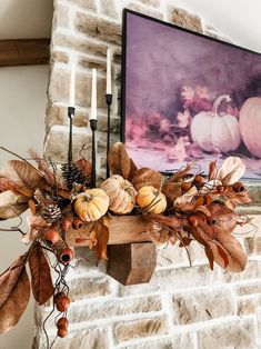 a fireplace mantle decorated with fall leaves and pumpkins, candlesticks and a painting