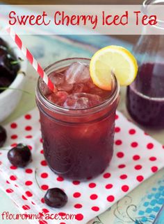 a drink in a mason jar with ice and cherries on the table next to it