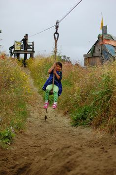 a woman sitting on top of a rope in the middle of a dirt road next to tall grass