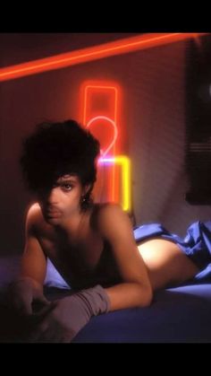 a woman laying on top of a bed next to a neon sign in the background