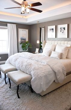 a large white bed sitting in a bedroom next to a window with curtains on it