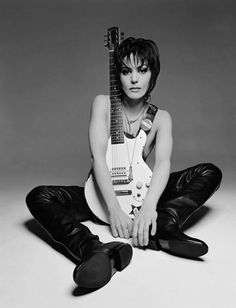 a woman sitting on the ground with a guitar in her hand and wearing black leather pants