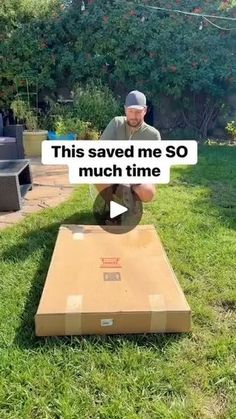 a man is sitting on top of a cardboard box in the grass and has his hand over it