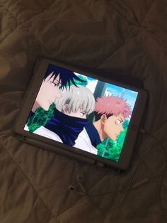 an ipad sitting on top of a bed next to another device with anime characters on the screen