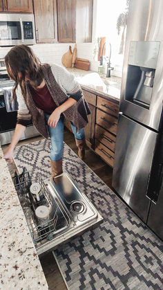 a woman bending over to pick something out of the dishwasher in her kitchen