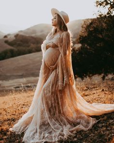 a pregnant woman wearing a long dress and hat standing in the middle of a field