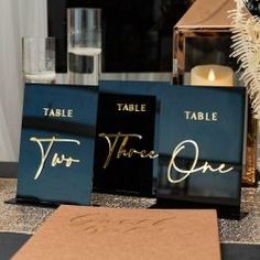 three black and gold table signs sitting on top of a table next to a candle