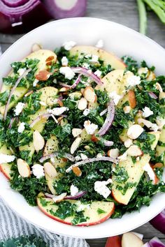 an apple and kale salad with feta cheese in a white bowl on a wooden table