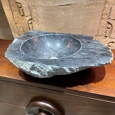 a stone bowl sitting on top of a wooden table next to a door handle and drawer