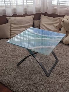 a glass coffee table sitting on top of a carpeted floor next to a teddy bear