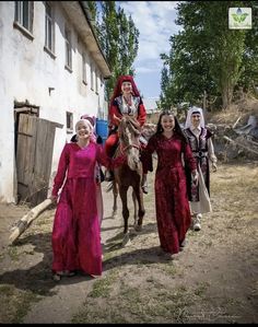 three women in red dresses are walking down the street with a horse and two men