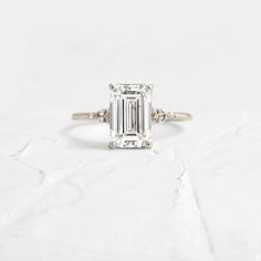 an emerald cut diamond ring with three diamonds on the band