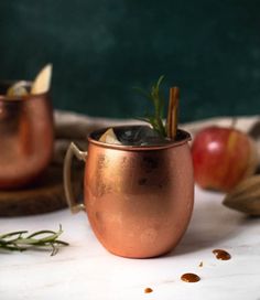 two copper mugs with cinnamon, apple and rosemary garnish on the side