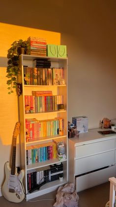 there is a book shelf with many books on it and a guitar next to it