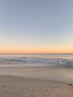 an empty beach with waves coming in from the ocean and footprints on the sand at sunset