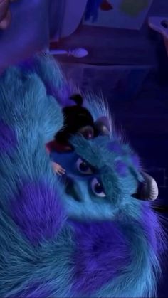 an animated blue furry animal laying on top of a purple floor next to a person