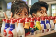 two people behind a row of bottles with different colored drinks in them and one person making the peace sign